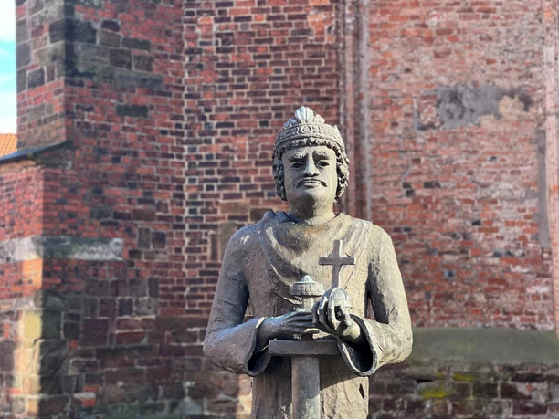 Steinfigur von Karl dem Großen vor einer Backsteinmauer, hält Kreuz und Modell einer Kirche in Händen.