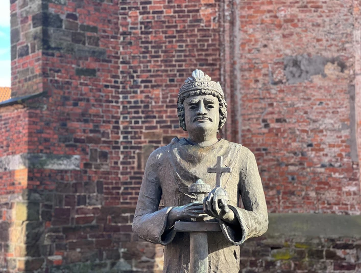 Steinfigur von Karl dem Großen vor einer Backsteinmauer, hält Kreuz und Modell einer Kirche in Händen.