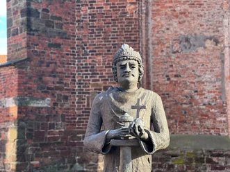 Karl der Große Steinfigur von Karl dem Großen vor einer Backsteinmauer, hält Kreuz und Modell einer Kirche in Händen.