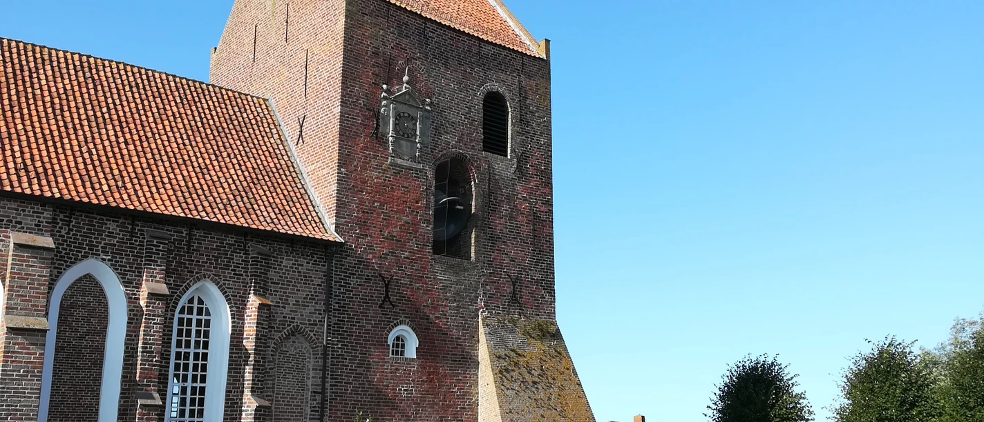 Kirche Groothusen Backsteinkirche mit hohem Turm und rotem Ziegeldach vor blauem Himmel, umgeben von Grabsteinen.
