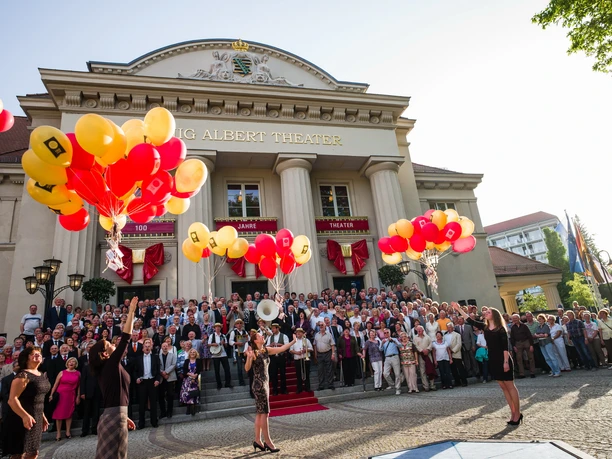 Group of people in front of the König Albert Theater Bad Elster, colorful balloons rise.