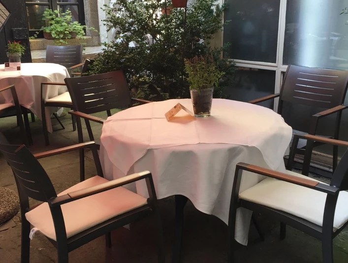 Ein runder Tisch mit weißer Tischdecke und vier modernen Stühlen in einem Außenbereich.