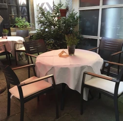 La Scala draußen Homepage.jpg Ein runder Tisch mit weißer Tischdecke und vier modernen Stühlen in einem Außenbereich.