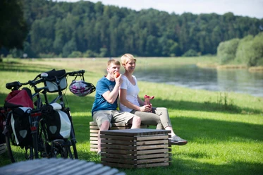 Picknick an der Weser Ein Paar genießt ein Picknick am Flussufer der Weser, umgeben von grüner Natur und Fahrrädern.