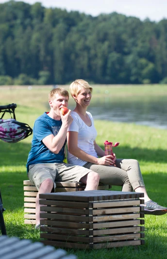 Picknick an der Weser Ein Paar genießt ein Picknick am Flussufer der Weser, umgeben von grüner Natur und Fahrrädern.