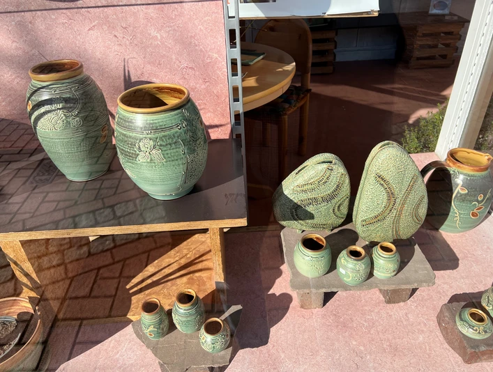 Verschiedene handgefertigte Keramikvasen und Objekte mit grüner Glasur und floralen Verzierungen.