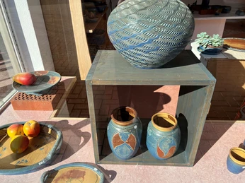 Zwei kunstvoll bemalte Keramiktöpfe und Schalen mit Früchten in einem sonnigen Schaufenster arrangiert.