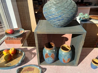 Keramikwerkstatt Luchtmann Zwei kunstvoll bemalte Keramiktöpfe und Schalen mit Früchten in einem sonnigen Schaufenster arrangiert.