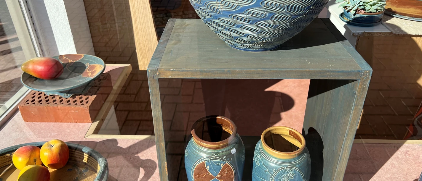 Keramikwerkstatt Luchtmann Zwei kunstvoll bemalte Keramiktöpfe und Schalen mit Früchten in einem sonnigen Schaufenster arrangiert.