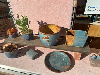 Keramikkunstwerke auf Holzregal nah betrachtet, Pflanzen und leuchtende Muster betonen handgefertigte Detailverliebtheit.