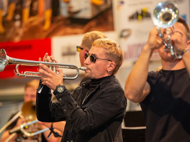 4096-2731-max (1).jpg Musiker mit Trompeten spielen intensiv auf einer Bühne bei einem Konzert.