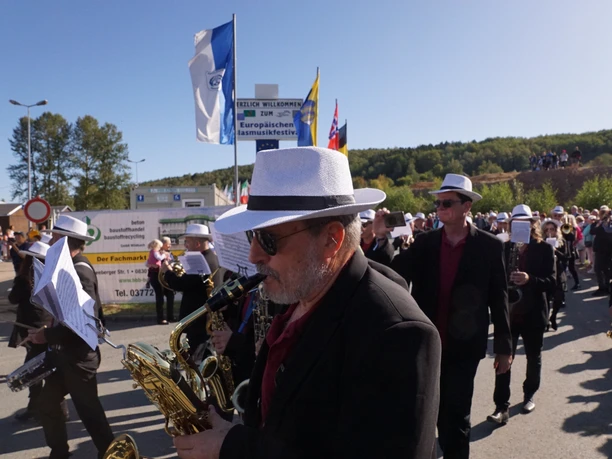 3008-2000-max.jpg Menschen in schwarzen Anzügen mit weißen Hüten und Blasinstrumenten bei einer Parade im Freien.