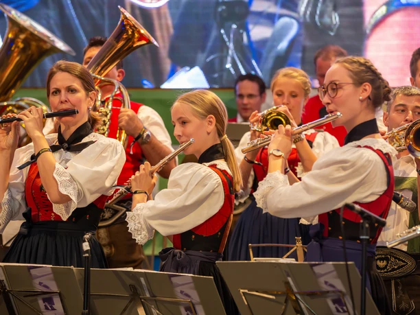 4096-2731-max.jpg Musikgruppe in traditioneller Tracht spielt Flöten und Blechblasinstrumente auf einer Bühne.