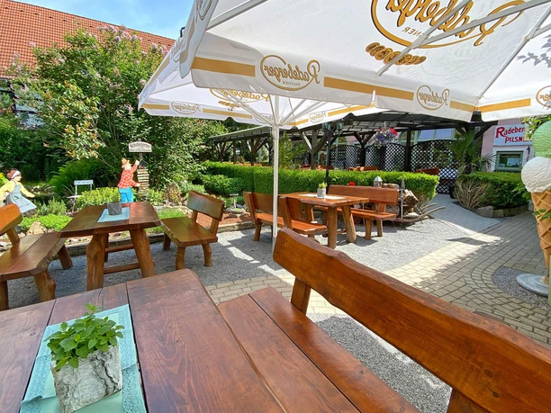 Wooden benches and tables under large parasols in a green beer garden; a large ice cream model in the background.