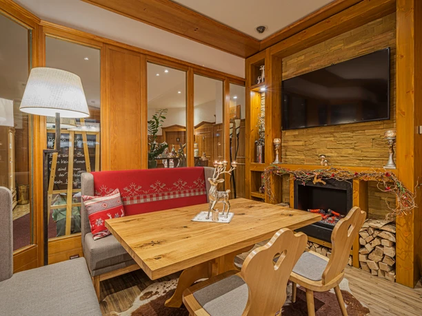 Augustusberg - Hotel & Restaurant Gemütlicher Raum mit Holzmöbeln, rotem Sofa, Kamin und Dekorationen; warme Beleuchtung und einladende Atmosphäre.
