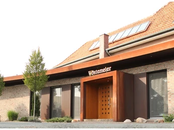 Gaststätte Wöstemeier_Außenansicht Modernes Gebäude mit Backsteinfassade, großem Holzportal und umgebenden Bäumen im Vordergrund.