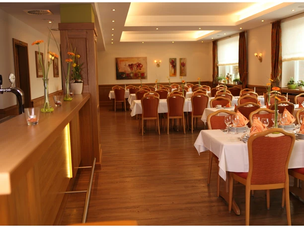 Eleganter Speiseraum mit gedeckten Tischen, orange Akzenten und einem langen Tresen aus Holz.