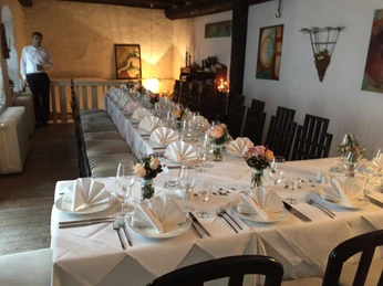 La Scala Essen Gruppe.JPG Ein festlich gedeckter langer Tisch mit weißer Tischdecke und Blumenarrangements in einem Restaurant.