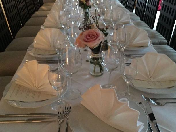 Elegant gedeckter Tisch mit weißen Servietten, Weingläsern und Rosenarrangement in der Mitte.