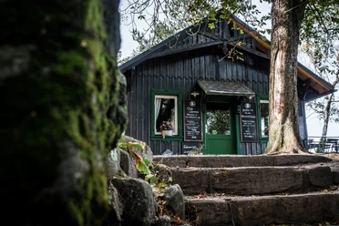Bergwirtschaft Papststein Sommer Capanna in legno con infissi e porta verdi, circondata da alberi; due tavoli con menu accanto all'ingresso, atmosfera autunnale.