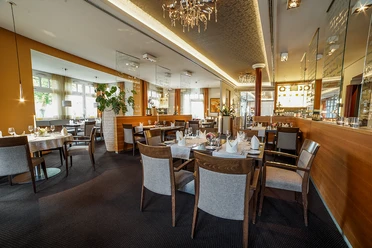 Ein stilvoll eingerichteter Restaurantraum mit elegant gedeckten Tischen und gemütlicher Atmosphäre.