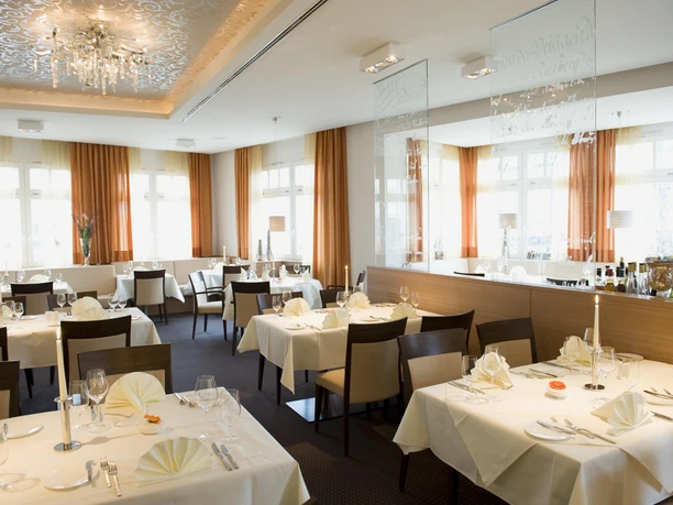 Elegantes Restaurant mit stilvoll gedeckten Tischen, in warmen Orangetönen und Kristallleuchter.
