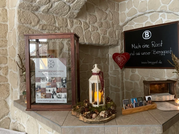 A display case with a poster "Winter Stories" stands on a stone counter, next to it a white lantern with a candle and a heart decoration on the wall.