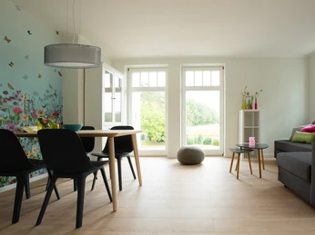 Geräumiger Ess- und Wohnbereich mit Holzboden, stilvollen Möbeln und Fensterfront zur Natur.