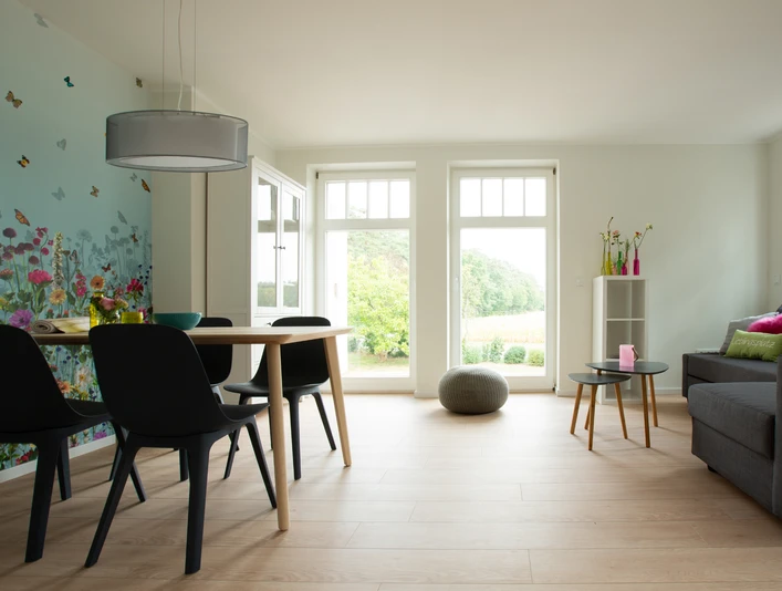 Geräumiger Ess- und Wohnbereich mit Holzboden, stilvollen Möbeln und Fensterfront zur Natur.