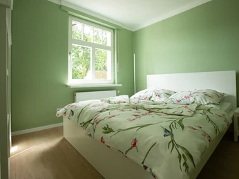 Blick in ein helles Schlafzimmer mit grünen Wänden, Blick auf Fenster und Blumenbettwäsche.