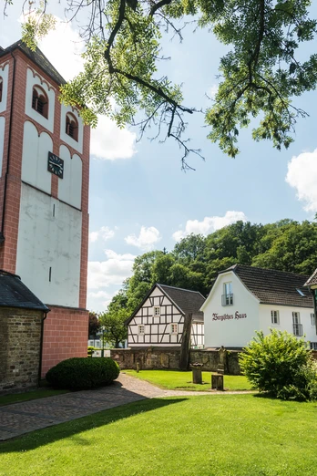 St. Pankratius Kirche Odenthal mit historischen Fachwerkhäusern und grünem Garten im Vordergrund.