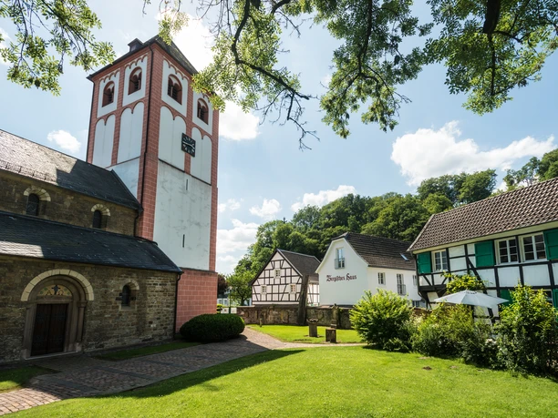St. Pankratius Kirche Odenthal mit historischen Fachwerkhäusern und grünem Garten im Vordergrund.