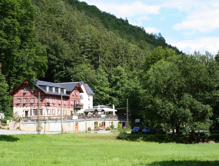 Restaurant Forsthaus im Kirnitzschtal Ein großes, rotes Gebäude mit weißen Fenstern steht am Waldrand, umgeben von grünen Bäumen und einer Wiese unter blauem Himmel.A large, red building with white windows stands on the edge of the forest, surrounded by green trees and a meadow under a blue sky.Na okraji lesa stojí velká červená budova s bílými okny, obklopená zelenými stromy a loukou pod modrou oblohou.Duży, czerwony budynek z białymi oknami stoi na skraju lasu, otoczony zielonymi drzewami i łąką pod błękitnym niebem.Een groot, rood gebouw met witte ramen staat aan de rand van het bos, omringd door groene bomen en een weiland onder een blauwe hemel.Un grande edificio rosso con finestre bianche si trova ai margini della foresta, circondato da alberi verdi e da un prato sotto un cielo azzurro.