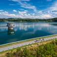 Große Dhünntalsperre Eine malerische Landschaft mit einem klaren See, Radfahrern und grünen Hügeln im Hintergrund unter blauem Himmel.