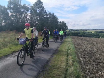 IMG_20210828_100354 Bier-Route-Kreis Höxter.jpg Eine Gruppe von Radfahrern in bunter Sportkleidung fährt auf einem schmalen, bewaldeten Weg.