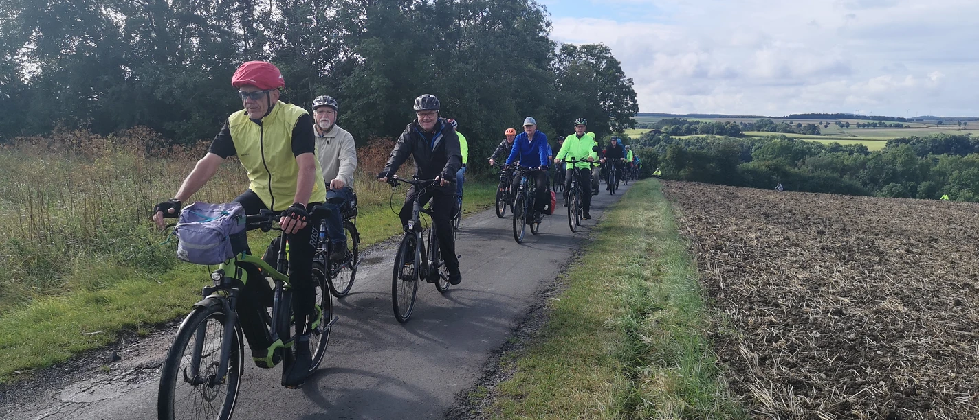 IMG_20210828_100354 Bier-Route-Kreis Höxter.jpg Eine Gruppe von Radfahrern in bunter Sportkleidung fährt auf einem schmalen, bewaldeten Weg.