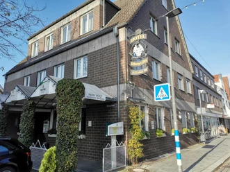 Hotel Vogt_Außenansicht Historisches Hotel mit Ziegelsteinfassade, weißem Vordach und grünem Efeu an der Front, daneben Geschäfte.