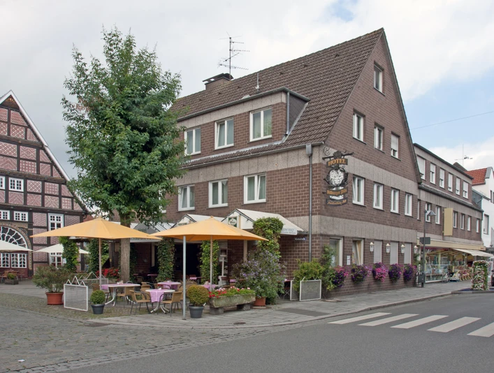 Ecke in einer deutschen Stadt mit Fachwerkhaus, Café mit gelben Schirmen und blühenden Pflanzen.