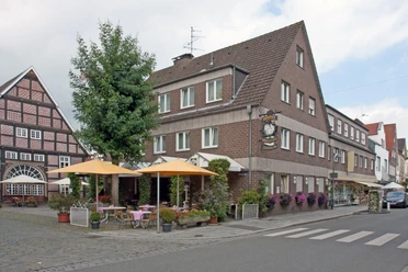 Hotel Vogt_Außenansicht Ecke in einer deutschen Stadt mit Fachwerkhaus, Café mit gelben Schirmen und blühenden Pflanzen.