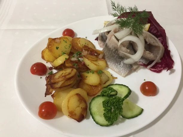 Hotel Vogt_Speisen Ein Teller mit geräuchertem Fisch, Zwiebeln, Bratkartoffeln, Gurke, Kirschtomaten und Kräutern.
