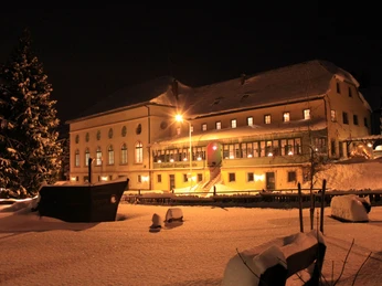 Gasthof Hertigswalde Winter Ein verschneiter Gasthof bei Nacht, beleuchtet von warmem Licht, mit einem großen, schneebedeckten Tannenbaum im Vordergrund.A snow-covered inn at night, illuminated by warm light, with a large, snow-covered Christmas tree in the foreground.Zasněžený noční hostinec osvětlený teplým světlem s velkým zasněženým vánočním stromem v popředí.Zajazd pokryty śniegiem w nocy, oświetlony ciepłym światłem, z dużą, pokrytą śniegiem choinką na pierwszym planie.Een besneeuwde herberg bij nacht, verlicht door warm licht, met een grote, besneeuwde kerstboom op de voorgrond.Una locanda innevata di notte, illuminata da una luce calda, con un grande albero di Natale innevato in primo piano.
