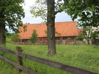 Historisches Fachwerkhaus auf abgelegenem Grundstück, von grünen Bäumen und Wiese umgeben.