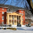 Parkhotel Bad Schandau Winter A large, two-tone building in red and yellow stands in a snowy landscape with trees and a blue sky in the background.