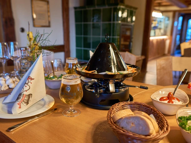 Essen vom heißen Hut Ein Tisch mit einem Tischgrill voller Gemüse, einem Glas Bier, Brotkorb und Schalen mit Dips in einem gemütlichen Raum.