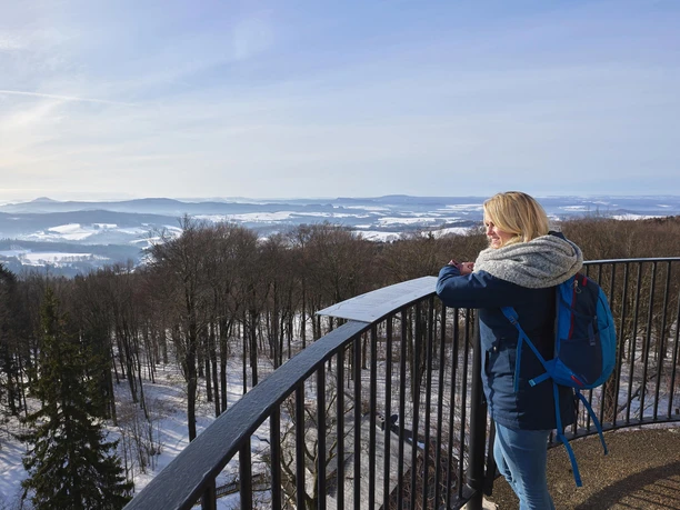 Uitzicht vanaf de Prinz Georg toren op de Ungerberg Vrouw met blauwe rugzak en grijze sjaal staat op een uitkijkpunt en kijkt uit over een besneeuwd landschap met bomen en heuvels.