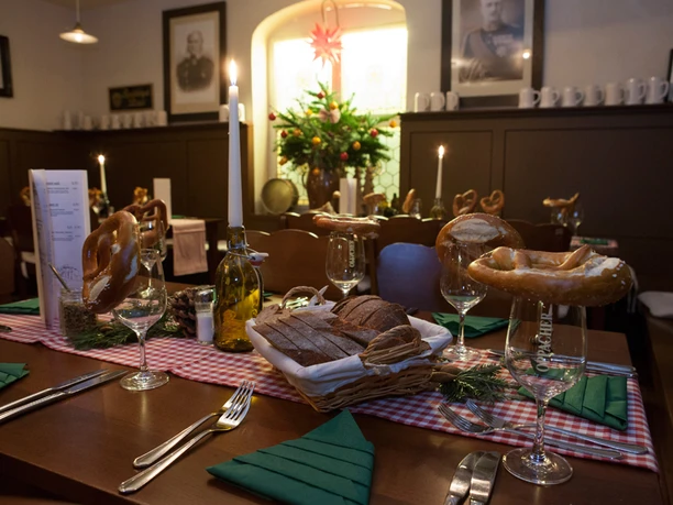 Důstojnická jídelna Restaurace Pevnost Königstein Slavnostně prostřený stůl v bavorské restauraci s preclíky na sklenicích, světlem svíček, chlebem a jedlovými větvičkami na červenobílém kostkovaném ubrusu.