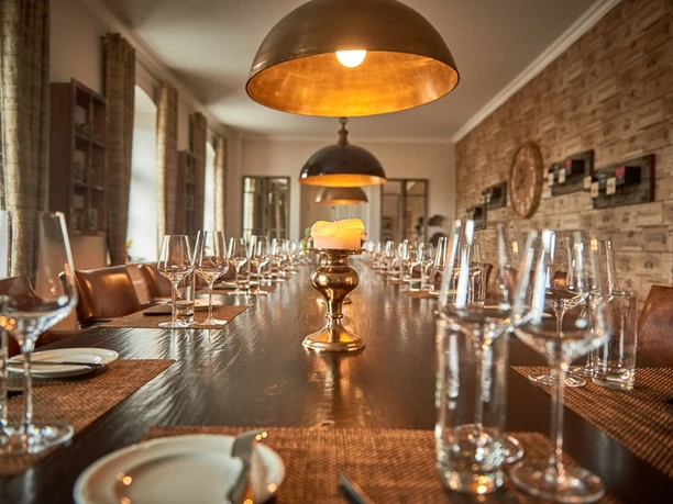 Café & Wine House Pražírna kávy Schmole v Pirně Elegantní prostřený jídelní stůl se sklenicemi na víno a talíři, osvětlený teplými zlatými závěsnými lampami ve stylové místnosti s dřevěnými stěnami.
