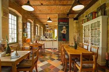 Gezellig café met houten tafels en stoelen, kleurrijke tegelvloer, bakstenen muren en nostalgische poster; warme, uitnodigende sfeer.