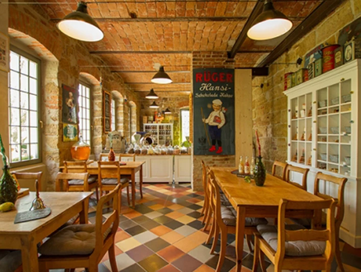 Gemütliches Café mit Holztischen und Stühlen, buntem Fliesenboden, Ziegelwänden und nostalgischem Poster; warme, einladende Atmosphäre.Cozy café with wooden tables and chairs, colorful tiled floor, brick walls and nostalgic poster; warm, inviting atmosphere.Útulná kavárna s dřevěnými stoly a židlemi, barevnou dlažbou, cihlovými zdmi a nostalgickým plakátem; příjemná atmosféra.Przytulna kawiarnia z drewnianymi stołami i krzesłami, kolorową podłogą wyłożoną kafelkami, ceglanymi ścianami i nostalgicznym plakatem; ciepła, zachęcająca atmosfera.Gezellig café met houten tafels en stoelen, kleurrijke tegelvloer, bakstenen muren en nostalgische poster; warme, uitnodigende sfeer.Accogliente caffetteria con tavoli e sedie in legno, pavimento in piastrelle colorate, pareti in mattoni e poster nostalgici; atmosfera calda e invitante.