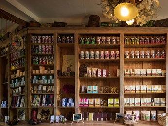 Holzregale in einem Laden, gefüllt mit bunten Verpackungen von Schokolade und Tee; warme, einladende Atmosphäre mit sanfter Beleuchtung.Wooden shelves in a store filled with colorful packages of chocolate and tea; warm, inviting atmosphere with soft lighting.Dřevěné police v obchodě plné barevných balíčků čokolády a čaje; příjemná atmosféra s měkkým osvětlením.Drewniane półki w sklepie wypełnione kolorowymi opakowaniami czekolady i herbaty; ciepła, zachęcająca atmosfera z delikatnym oświetleniem.Houten planken in een winkel vol kleurrijke verpakkingen van chocolade en thee; warme, uitnodigende sfeer met zachte verlichting.Scaffali in legno in un negozio pieno di confezioni colorate di cioccolato e tè; atmosfera calda e invitante con luci soffuse.